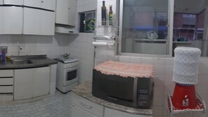 Une cuisine avec des armoires blanches, un évier, une cuisinière et un four à micro-ondes. Il y a une fenêtre donnant sur l’extérieur.