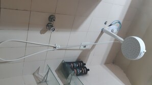 Un espace douche équipé d’un pommeau de douche à main, d’un robinet mural et d’un flacon de shampoing.