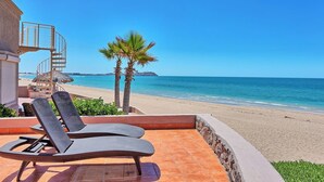 A beachside patio with two lounge chairs, a spiral staircase, and a view of the ocean.