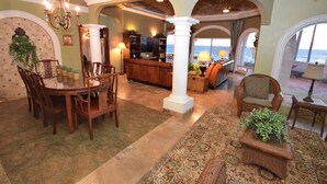 A spacious living area with a dining table, chairs, a sofa, and a view of the ocean.