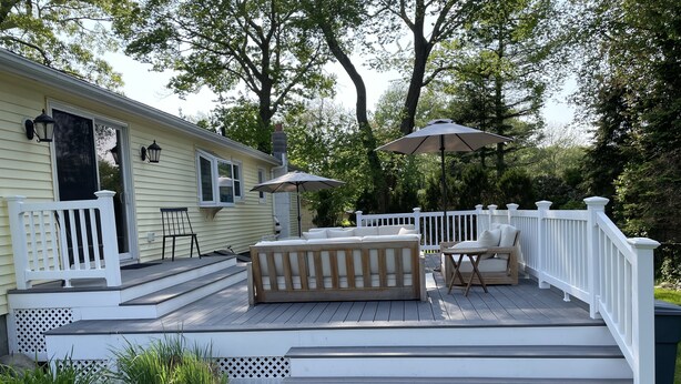Eine Terrasse mit Gartenmöbeln, einem weißen Geländer und einem überdachten Bereich mit Sonnenschirmen.