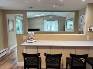 A kitchen with a white countertop, three black chairs, a bag of chips, and a large mirror reflecting the room.