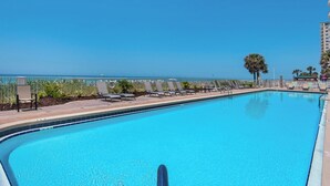 A clear blue pool with lounge chairs and a view of the ocean.