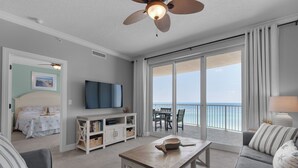 A spacious living room with a large sliding glass door leading to a balcony with a view of the ocean.