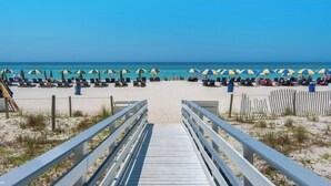 A beach with a wooden walkway leading to the shore, rows of beach chairs, and umbrellas.