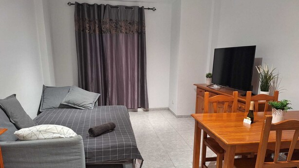 A bedroom with a bed, a bedside table with a TV, a small table with a bottle, and a chair. - Las Galletas 2A, sun, beach, relaxation (Las Galletas)