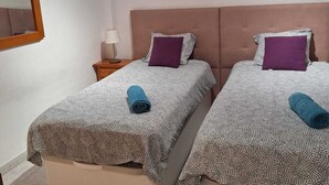 A room with two beds, each with a patterned bedspread and a pillow. There is a nightstand with a lamp between the beds. - Las Galletas 2A, sun, beach, relaxation (Las Galletas)