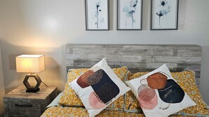 Une chambre à coucher avec une tête de lit en bois, une table de chevet avec une lampe et trois œuvres d’art florales accrochées au mur.