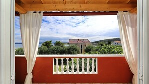A balcony with a view of a lake and buildings, wooden ceiling, and a red wall with a white balustrade. - Apartments Saphron Beach (Pasman)