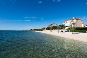 Ein Strandgrundstück mit klarem Wasser, einem Sandstrand und einem großen Gebäude mit mehreren Balkonen.