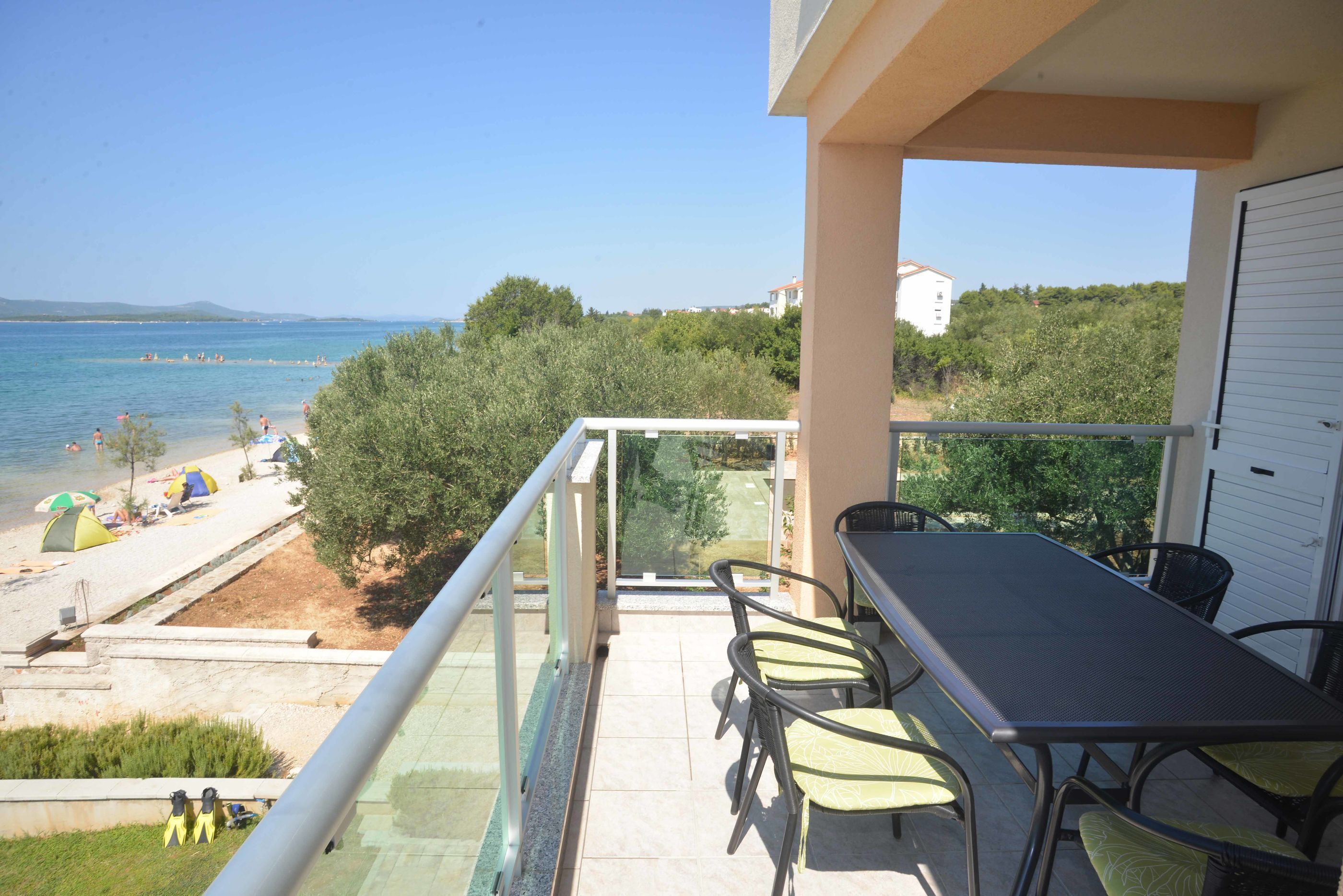 A balcony with a table and chairs, overlooking a beach with people and tents.
