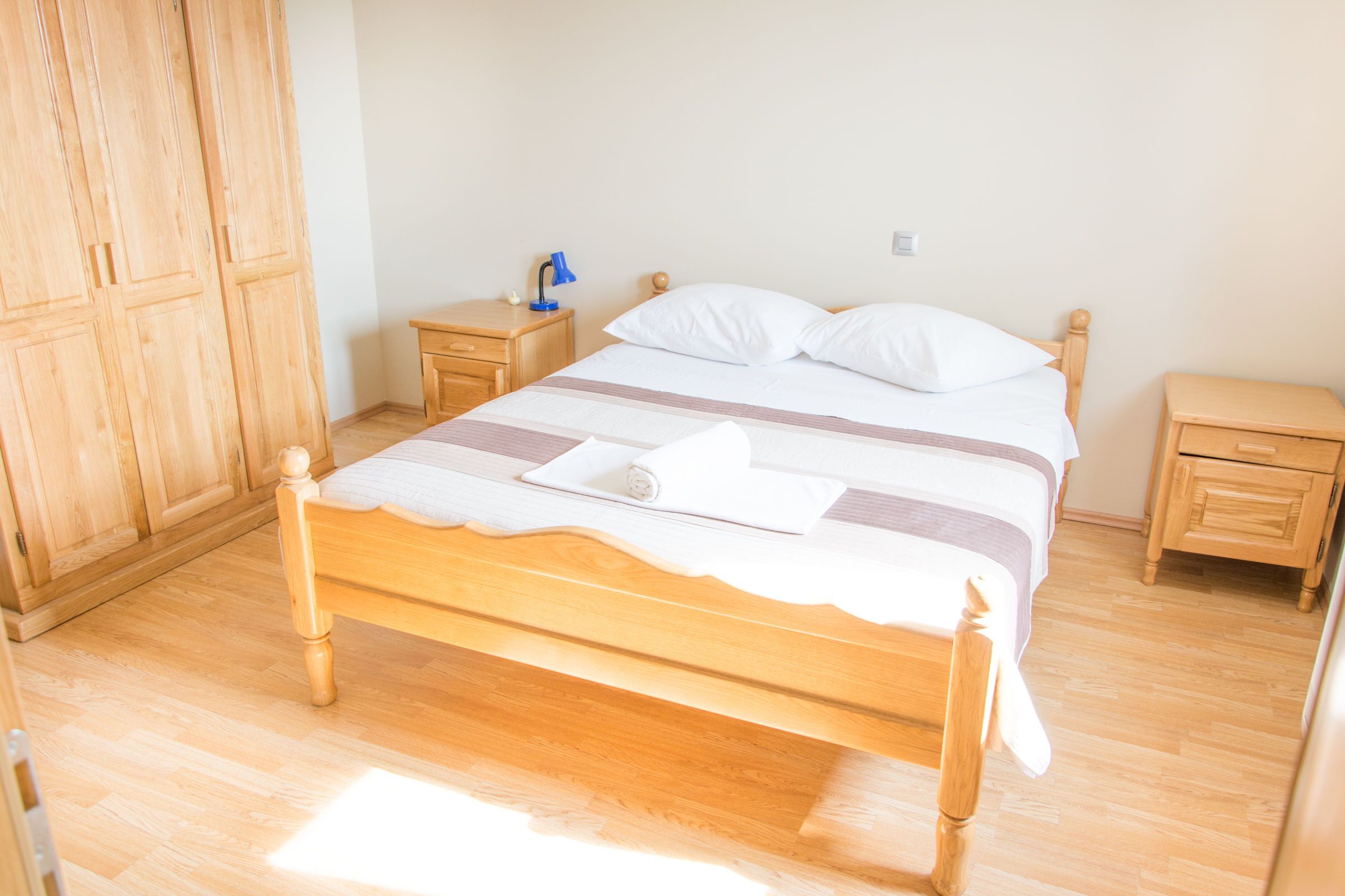 A neatly made bed with a striped bedspread, wooden headboard, and a bedside table with a lamp.