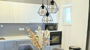 A modern dining area with a marble table, grey upholstered chairs, a vase with dried flowers, and pendant lighting. - Apartment Svabo (Dolac)