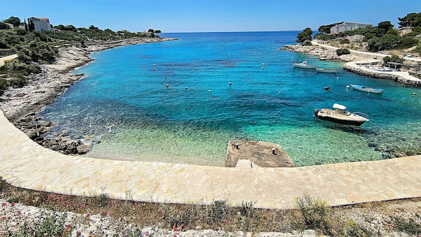 A coastal view with clear turquoise waters, boats, and rocky terrain. - Apartment Svabo (Dolac)