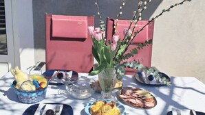 A table set outdoors with various dishes, a vase with flowers, and a pink chair. - Apartment Svabo (Dolac)