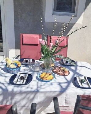 Ett bord dukat utomhus med olika rätter, en vas med blommor och en rosa stol.