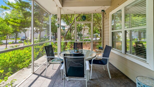 A covered patio with a table and chairs, large windows, and a ceiling fan. - Beach Cottage 120 at Hidden Dunes by Best Beach Getaways (Miramar Beach)