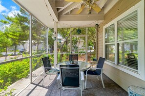 Eine überdachte Terrasse mit Tisch und Stühlen, großen Fenstern und einem Deckenventilator.