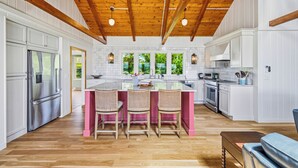 Une cuisine moderne avec des meubles blancs, un plafond en bois et un îlot central doté de chaises.