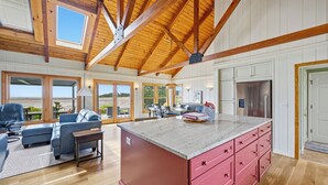 Une cuisine spacieuse dotée d’un grand îlot central, de poutres en bois et offrant une vue sur l’extérieur.