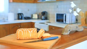 A kitchen with wooden cabinets, a countertop, a loaf of bread, a knife, and a decorative bird sculpture. - SeaSunrise: Modern, spacious Apt, A/C, WiFi, Near beach (Perama)