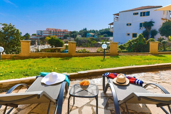 A terrace with two lounge chairs, a small table, and a bowl of oranges. - SeaSunrise: Modern, spacious Apt, A/C, WiFi, Near beach (Perama)