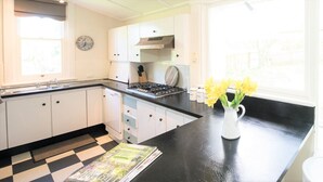 A kitchen with white cabinets, a black countertop, a gas stove, and a window with a view of greenery. - Casa Antica, 200m walk to Bowral Township, family friendly and strictly NO PETS! (Bowral)