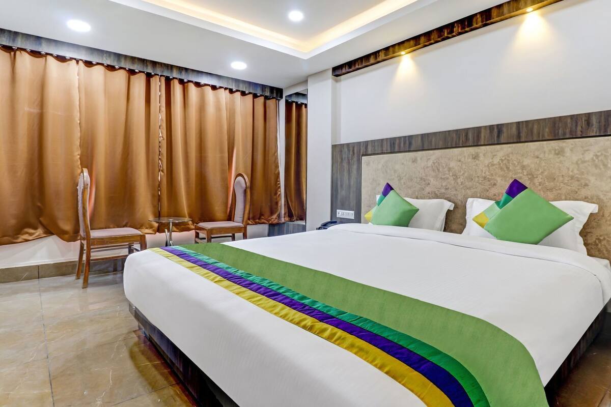 A hotel room with a large bed, a headboard with a textured design, a bedside table with a phone, and a curtain with a scalloped edge.