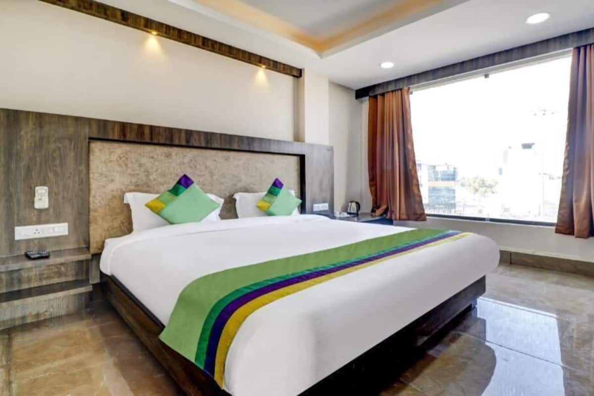 A hotel room with a large bed, a headboard, a window with curtains, and a view of the city.