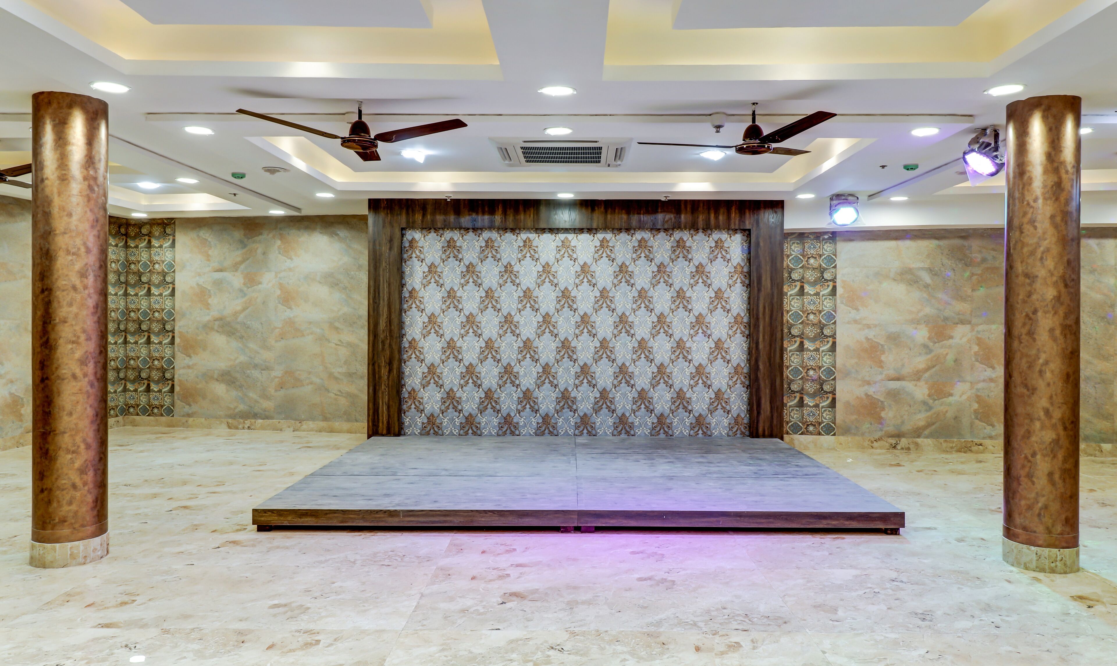 A spacious room with a stage, ceiling fans, and patterned walls.