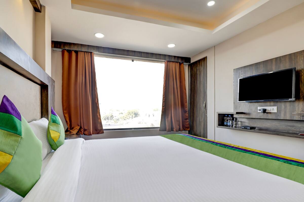 A hotel room with a large bed, a flat-screen TV, and a window with curtains.