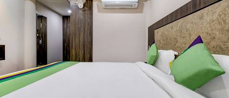 A hotel room with a bed, a ceiling fan, an air conditioning unit, and a wooden wardrobe.