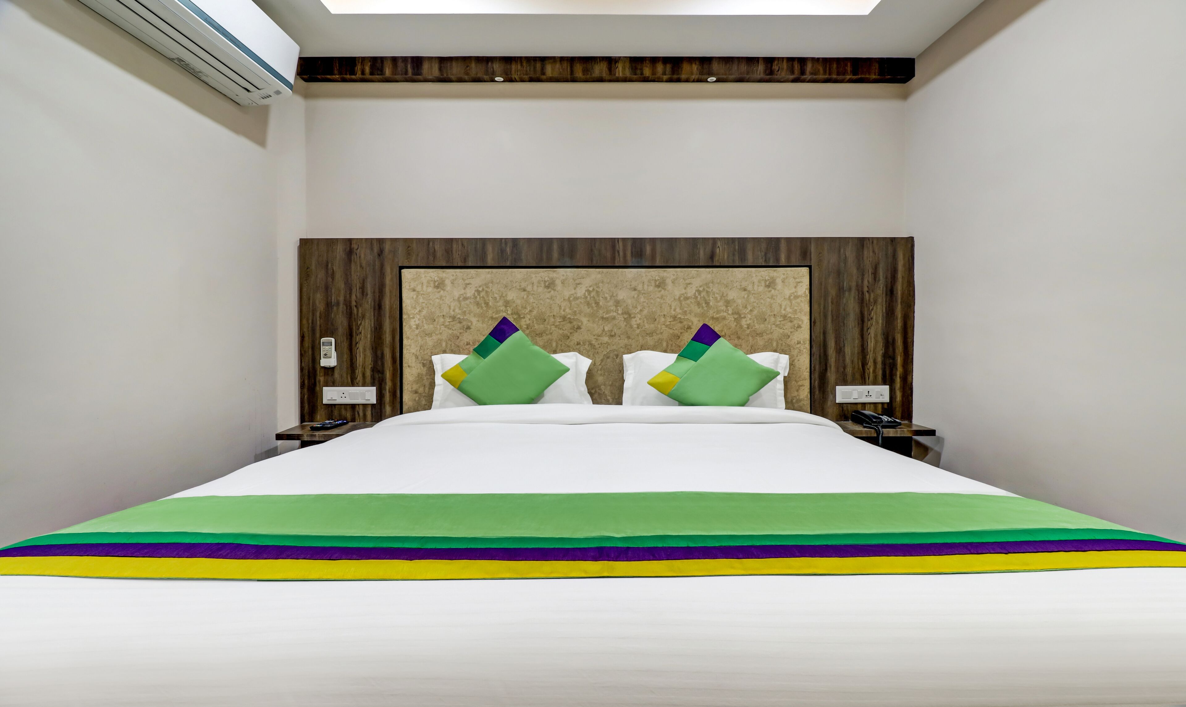 Une chambre d’hôtel moderne dotée d’un grand lit, de deux tables de chevet, d’un téléphone fixé au mur et d’un système de climatisation intégré.