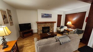 Ein Wohnzimmer mit Kamin aus Stein, einem Fernseher, einer Couch und einer Lampe.