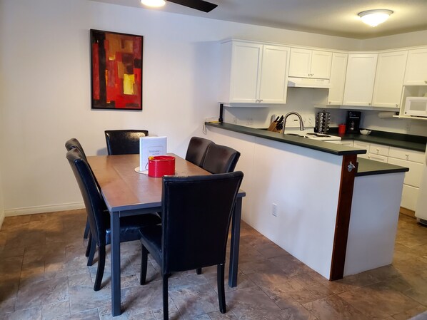 A modern kitchen with white cabinets, a black countertop, and a dining area with a wooden table and black chairs.