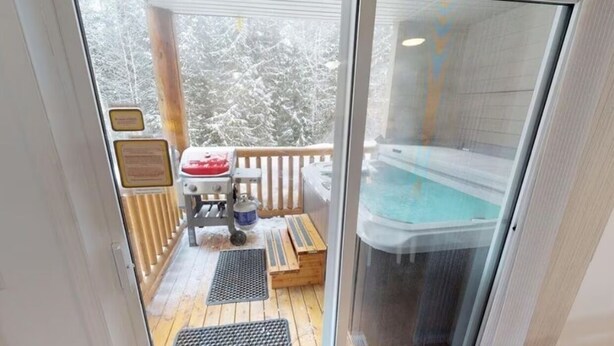 Ein durch Glas geschützter Balkon mit Whirlpool, Holzterrasse und einem kleinen Tisch mit Stühlen.
