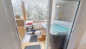 A glass-enclosed balcony with a hot tub, wooden deck, and a small table with chairs.
