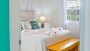 Ein Schlafzimmer mit einem Bett, einer Sitzbank, einem Deckenventilator, einem Fenster und Blick ins Grüne.