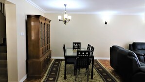A dining area with a glass table, black chairs, a wooden cabinet, and a patterned rug. - City of the Sun Newly renovated loving house (Nairobi)