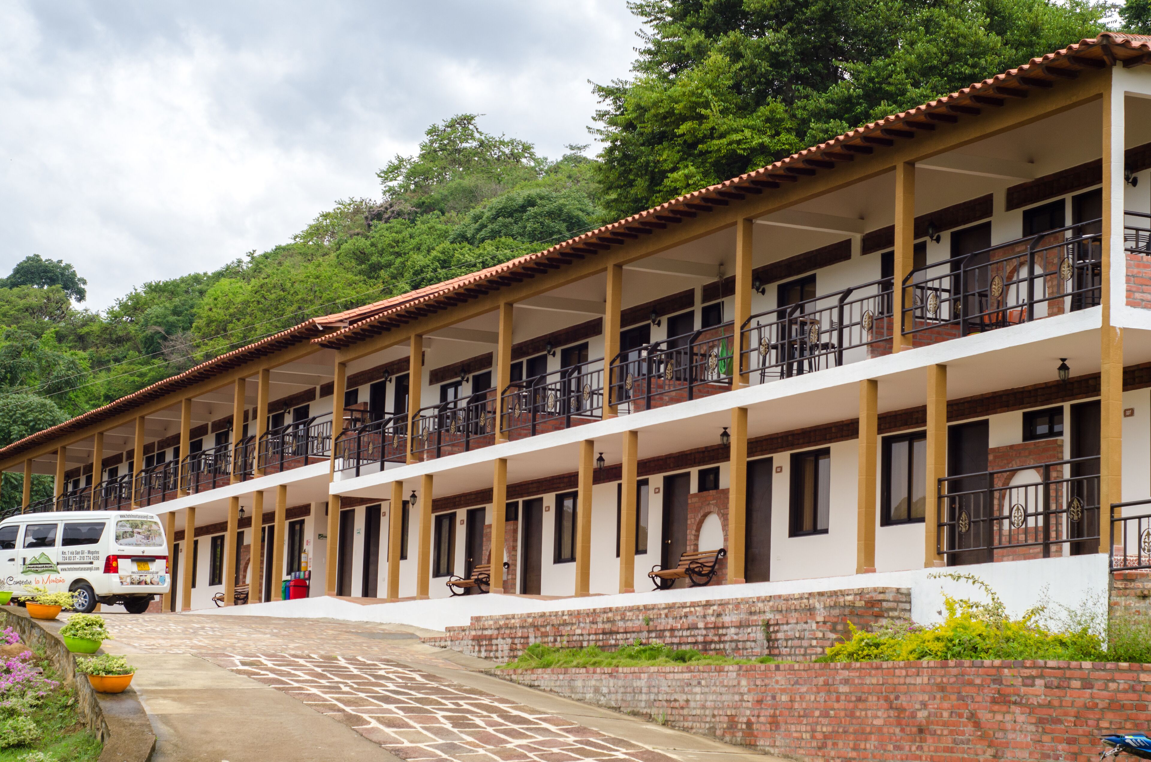 A multi-story hotel with balconies, a paved walkway, and a van parked in front.