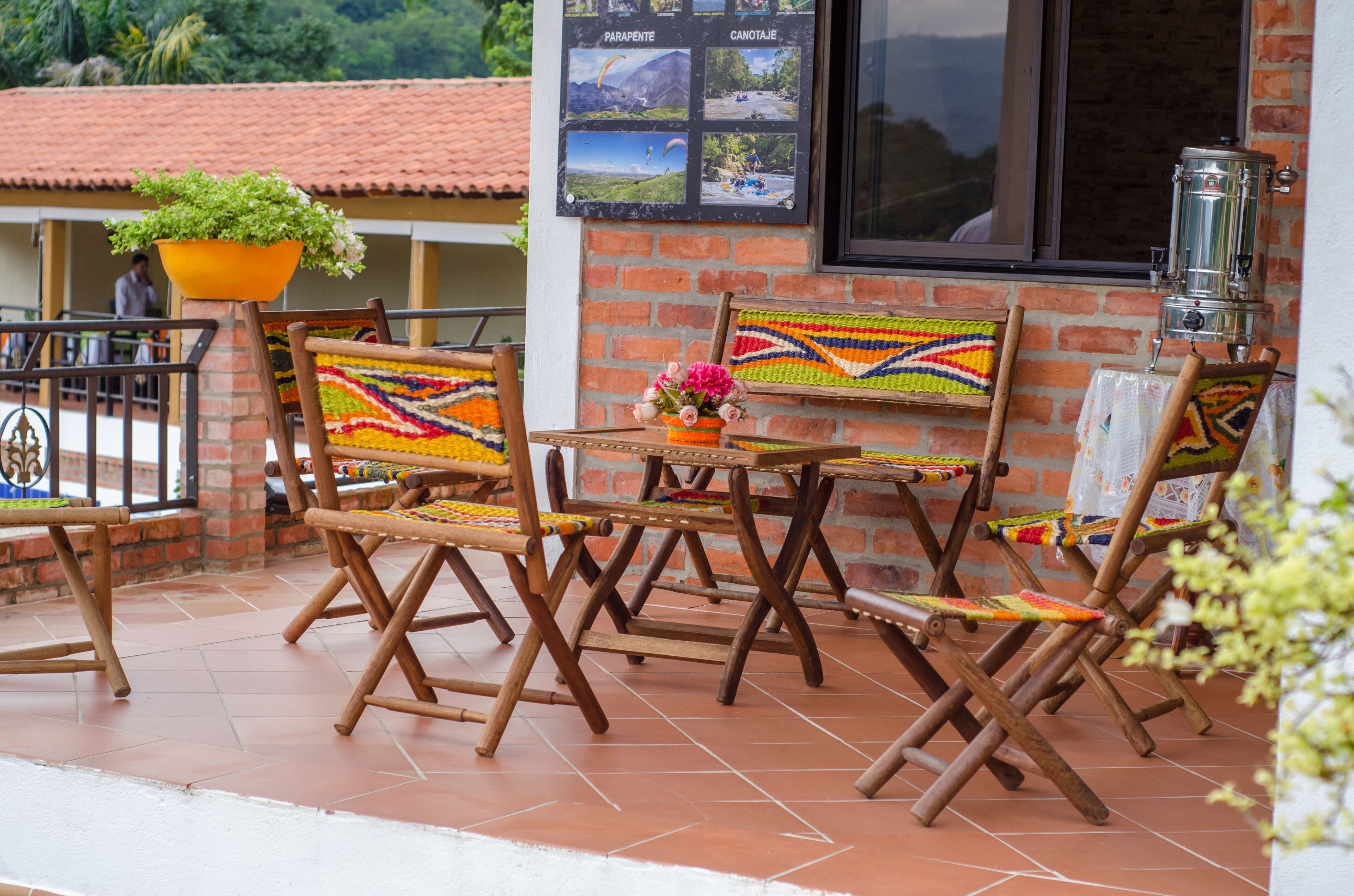 A patio with wooden chairs and tables, a brick wall, and a window with a view of the mountains.