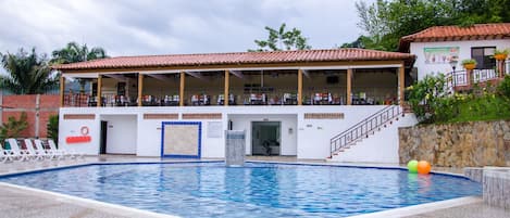 A swimming pool with a covered area, lounge chairs, and a staircase leading to a building with a tiled roof.