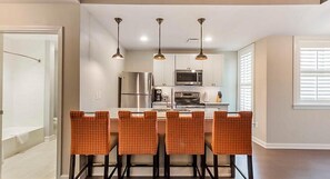Una cocina moderna con electrodomésticos de acero inoxidable, una isla central con taburetes de bar e iluminación colgante.