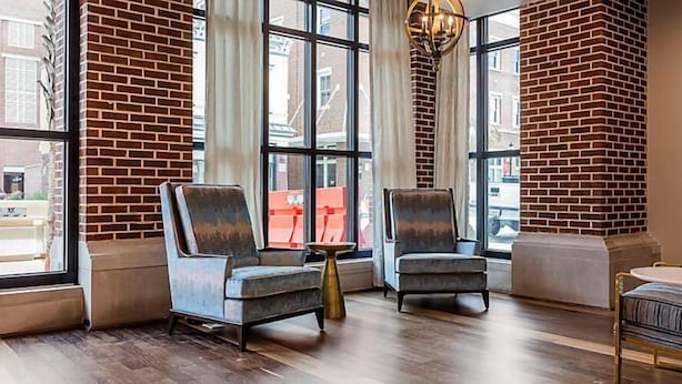 A modern interior with two armchairs, a small table, and a bench. Large windows provide views of the outside.