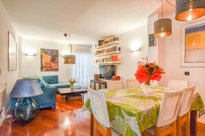 A well-lit living room with a dining area, a bookshelf, and a painting on the wall. - Apartment Mimi (Biograd)