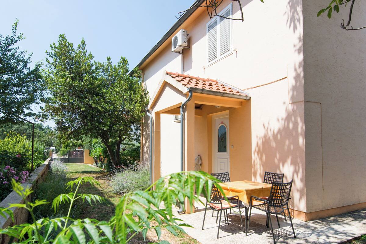 Ein Haus mit Terrasse, einem Tisch mit Stühlen und einem Garten mit Bäumen und Pflanzen.