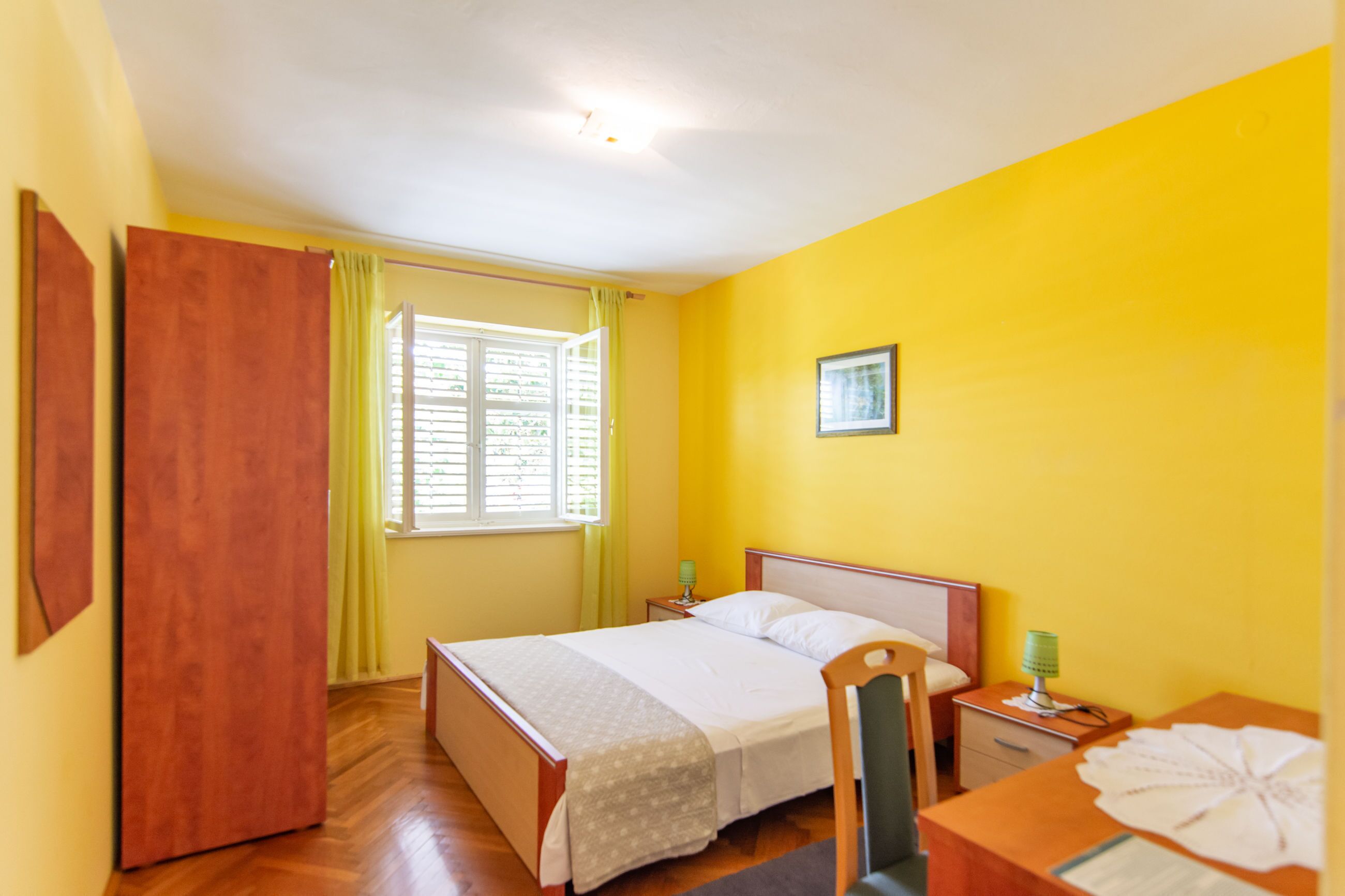 Une chambre à coucher avec un lit, une table de chevet, une chaise, un bureau et une fenêtre avec des rideaux.