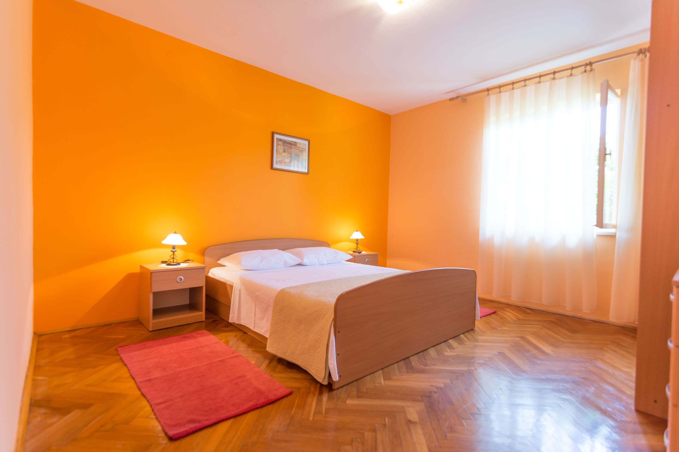 Ein Schlafzimmer mit einem Bett, Nachttischen, einem roten Teppich und einem Fenster mit Vorhängen.