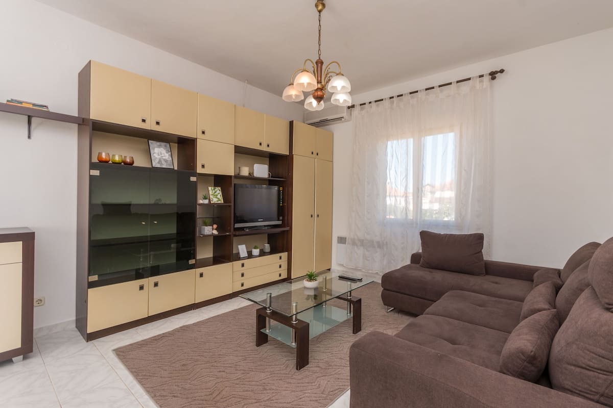 Uma sala de estar moderna com uma mesa de centro de vidro, sofá marrom e televisão embutida.