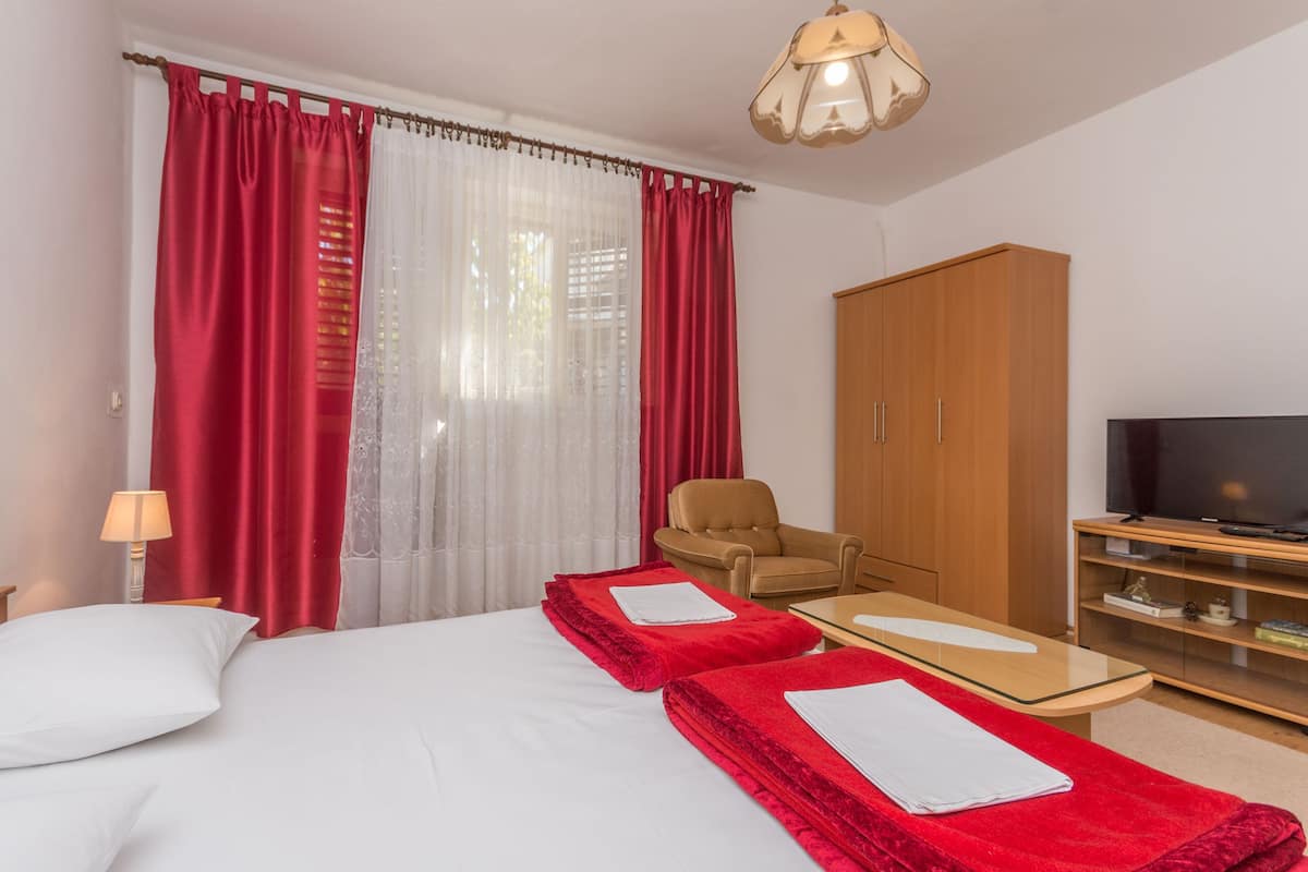 Quarto de hotel com uma cama, duas toalhas vermelhas, uma cadeira, uma televisão e um guarda-roupa.
